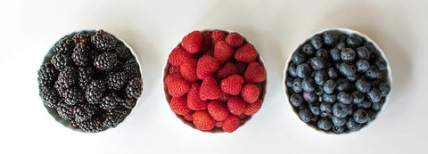Three bowls of blackberries, raspberries, and blueberries on a white background